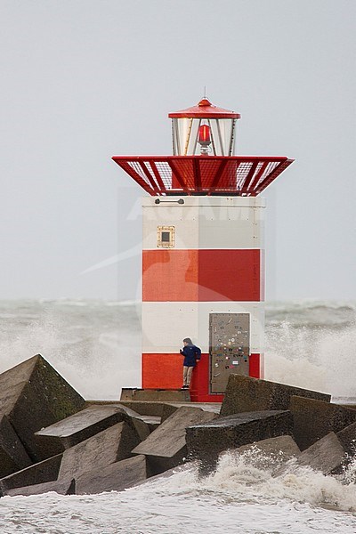 Jongen staat bij vuurtoren op pier tijdens storm; Boy standing next to lighthouse on jetty during storm stock-image by Agami/Menno van Duijn,